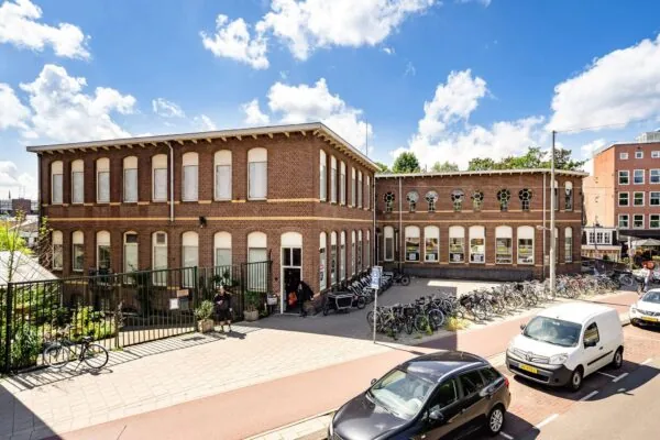 Bakstenen schoolgebouw aan de Admiraal de Ruijterweg met fietsenrekken en geparkeerde auto's op een zonnige dag.